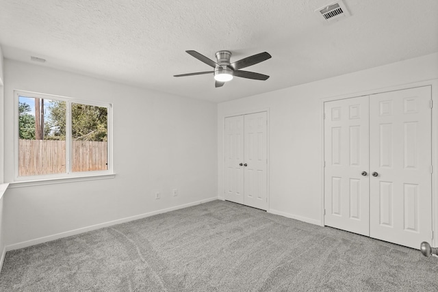 unfurnished bedroom with a textured ceiling, ceiling fan, carpet floors, and two closets