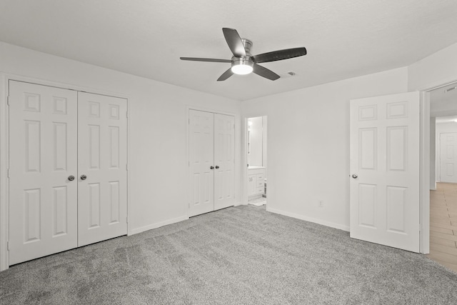 unfurnished bedroom featuring light carpet, ensuite bath, ceiling fan, and multiple closets