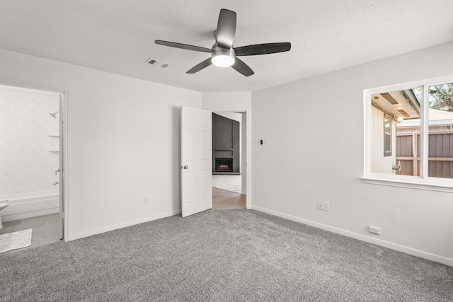 unfurnished bedroom with carpet flooring, ensuite bathroom, ceiling fan, and a brick fireplace