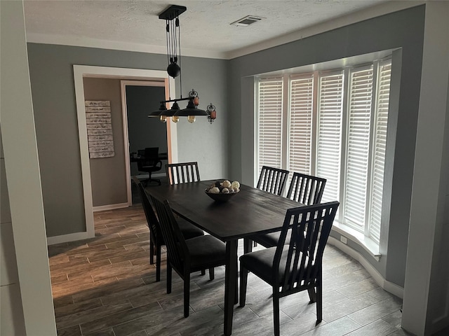 dining space with a textured ceiling, wood finish floors, visible vents, and baseboards