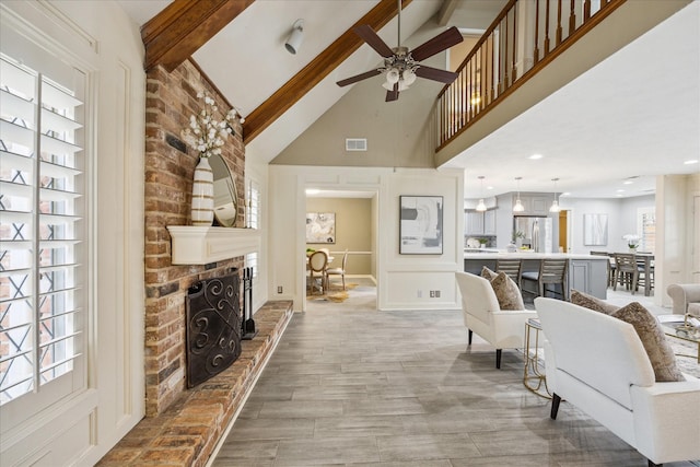 living room featuring beam ceiling, ceiling fan, a brick fireplace, and a wealth of natural light