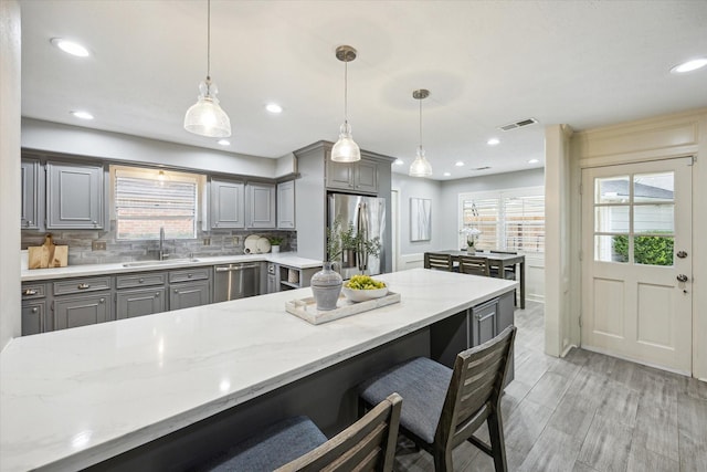 kitchen with light stone countertops, hanging light fixtures, stainless steel appliances, a kitchen bar, and sink