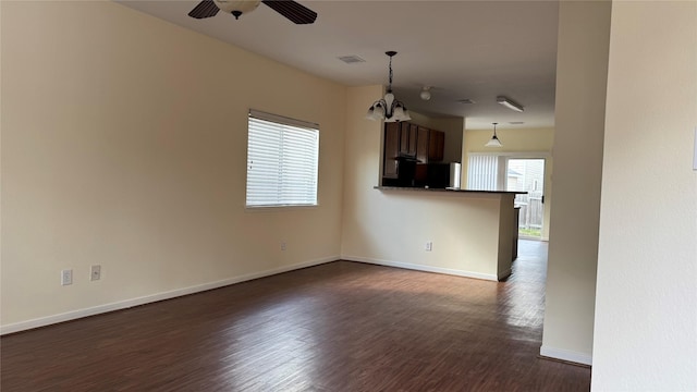 unfurnished living room with ceiling fan with notable chandelier, dark hardwood / wood-style flooring, and a wealth of natural light