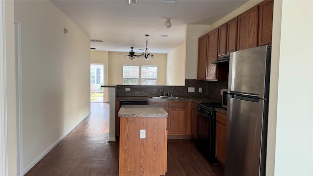 kitchen featuring stainless steel refrigerator, a center island, sink, black gas stove, and decorative light fixtures