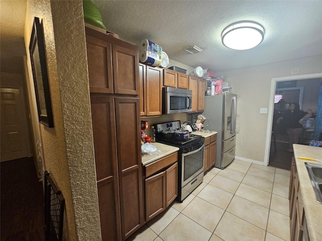 kitchen with sink, light tile patterned floors, stainless steel appliances, and a textured ceiling