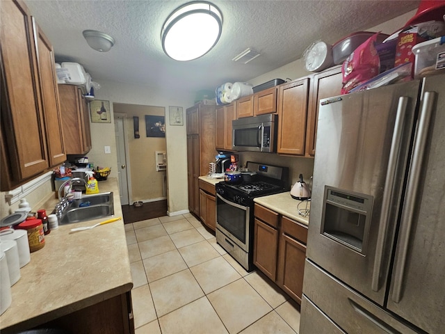 kitchen featuring appliances with stainless steel finishes, a textured ceiling, light tile patterned floors, and sink