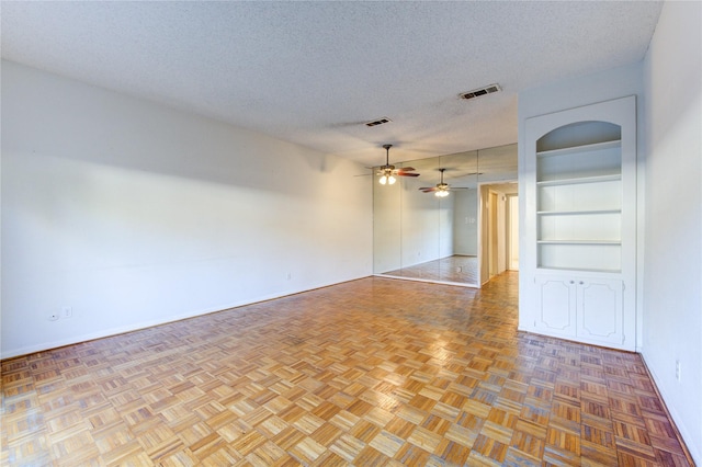 unfurnished room with ceiling fan, light parquet floors, a textured ceiling, and built in shelves