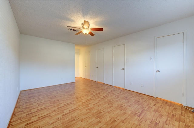 unfurnished bedroom featuring a textured ceiling, light wood-type flooring, ceiling fan, and multiple closets