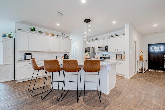 kitchen with white cabinets, an island with sink, light stone counters, and stainless steel appliances