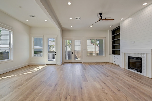 unfurnished living room with french doors, ceiling fan, built in features, light hardwood / wood-style floors, and a tiled fireplace