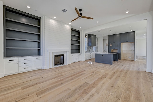 unfurnished living room featuring ceiling fan, light wood-type flooring, a fireplace, and built in shelves