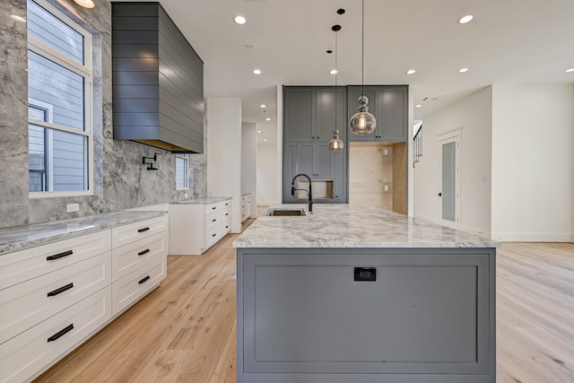 kitchen with decorative light fixtures, decorative backsplash, sink, and a kitchen island with sink