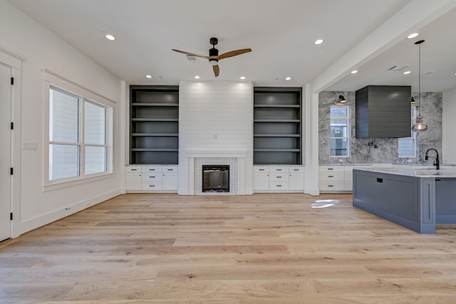 unfurnished living room with built in shelves, light hardwood / wood-style floors, a brick fireplace, and ceiling fan