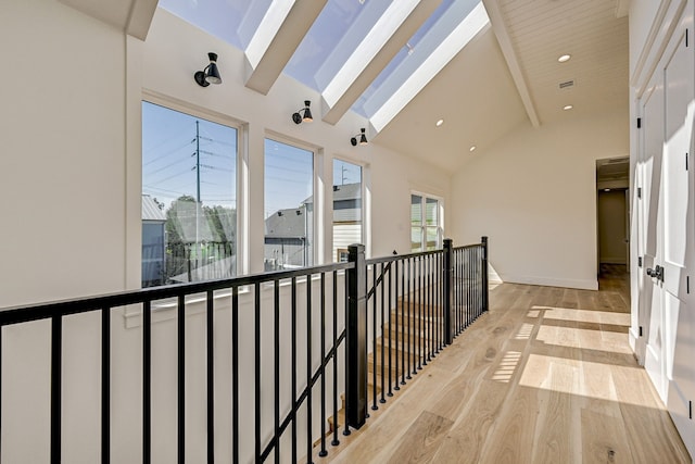 corridor featuring beam ceiling, light hardwood / wood-style floors, high vaulted ceiling, and a skylight