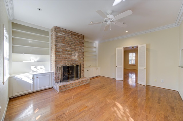 unfurnished living room featuring light hardwood / wood-style floors, ceiling fan, ornamental molding, a fireplace, and built in shelves