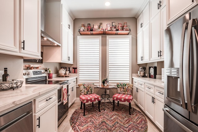 kitchen with wall chimney exhaust hood, light stone counters, white cabinetry, and appliances with stainless steel finishes