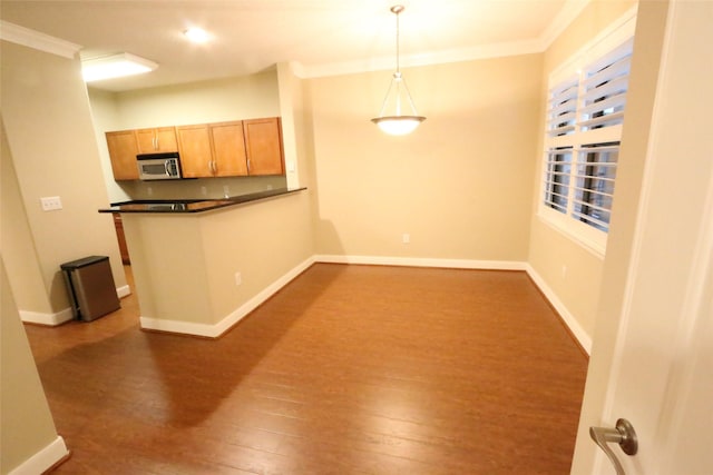 kitchen with kitchen peninsula, dark hardwood / wood-style flooring, hanging light fixtures, and ornamental molding