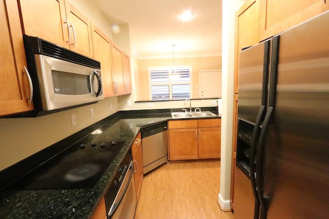 kitchen featuring sink, light hardwood / wood-style flooring, dark stone counters, pendant lighting, and appliances with stainless steel finishes