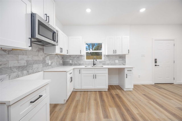 kitchen featuring white cabinets, decorative backsplash, light wood-type flooring, and sink