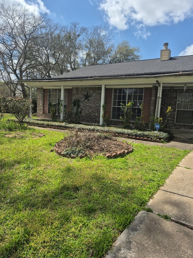 single story home featuring brick siding, a chimney, and a front lawn