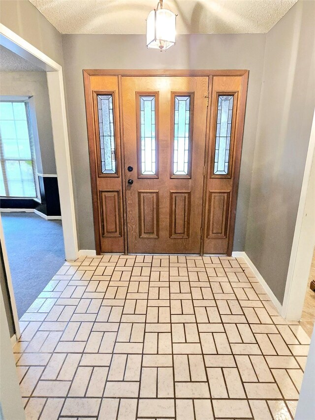 entryway featuring a textured ceiling, light colored carpet, and a notable chandelier