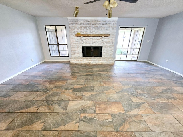 unfurnished living room with a brick fireplace, a textured ceiling, a healthy amount of sunlight, and ceiling fan