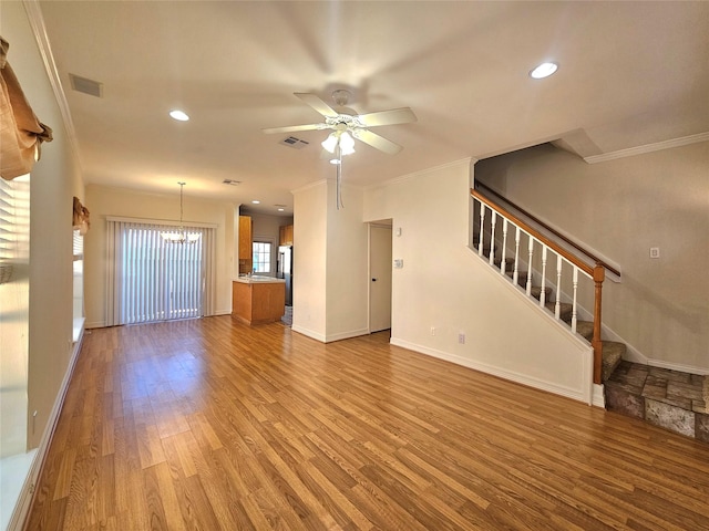 unfurnished living room featuring light wood-type flooring, ceiling fan with notable chandelier, and crown molding