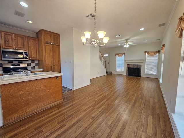 kitchen featuring dark hardwood / wood-style flooring, pendant lighting, decorative backsplash, ceiling fan with notable chandelier, and ornamental molding