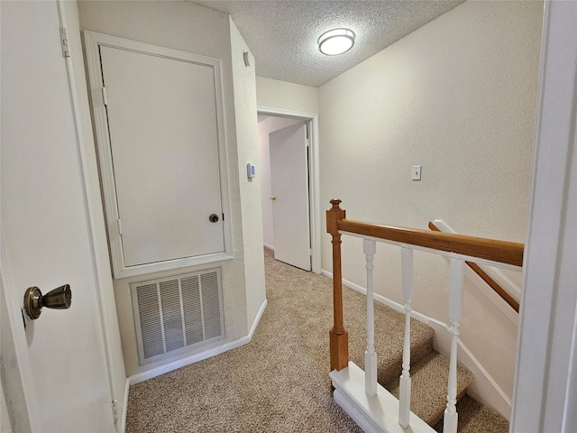 hallway with a textured ceiling and light colored carpet