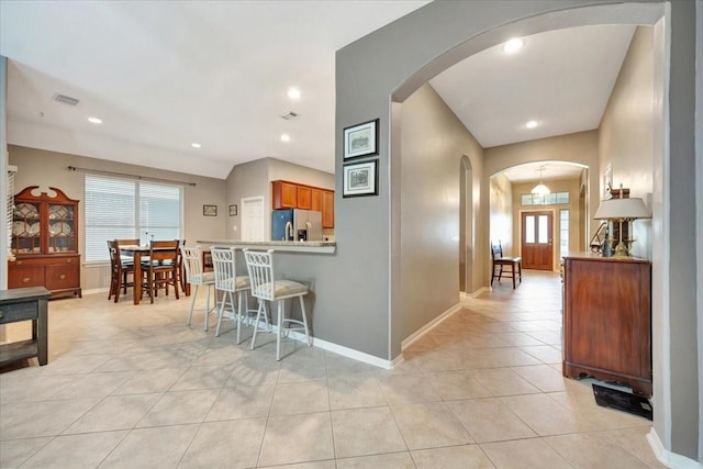 kitchen featuring light tile patterned flooring, light stone counters, kitchen peninsula, and stainless steel refrigerator with ice dispenser