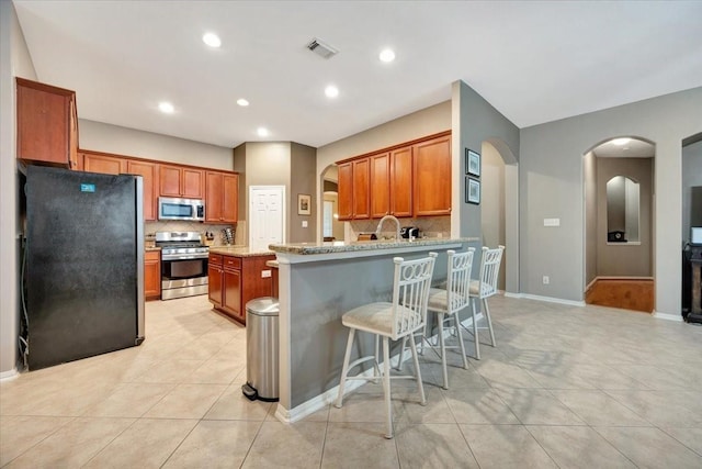 kitchen with light stone countertops, stainless steel appliances, a kitchen bar, decorative backsplash, and light tile patterned floors