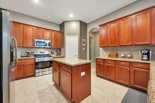 kitchen with light stone countertops, a kitchen island, stainless steel appliances, and light tile patterned floors