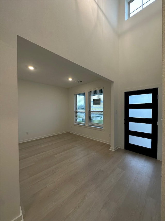 entryway with a wealth of natural light, a towering ceiling, and light wood-type flooring