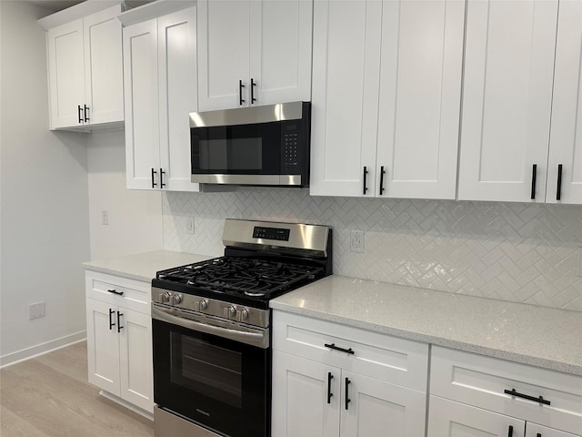 kitchen with white cabinetry, light stone countertops, backsplash, light hardwood / wood-style floors, and appliances with stainless steel finishes