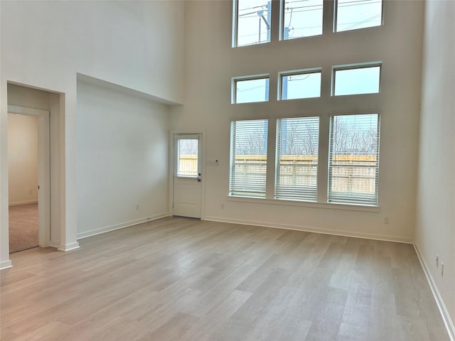 unfurnished living room with a high ceiling, light wood-type flooring, and plenty of natural light