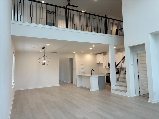 unfurnished living room featuring a high ceiling, light wood-type flooring, ceiling fan, and sink