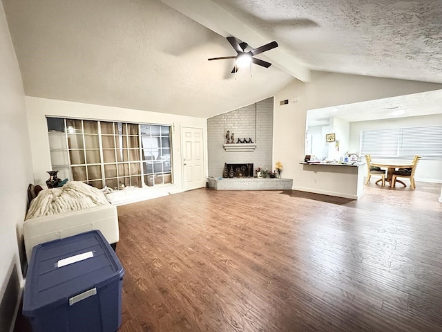 living room with hardwood / wood-style floors, lofted ceiling with beams, a brick fireplace, ceiling fan, and a textured ceiling