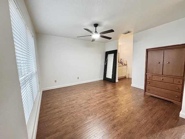 unfurnished bedroom with a textured ceiling, ceiling fan, ensuite bathroom, and dark wood-type flooring