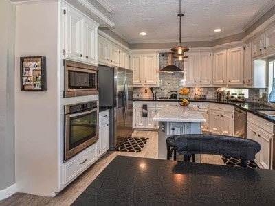 kitchen featuring appliances with stainless steel finishes, wall chimney range hood, decorative light fixtures, white cabinets, and a center island