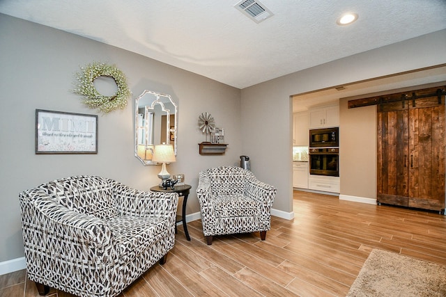 living area with a barn door, a textured ceiling, and light wood-type flooring