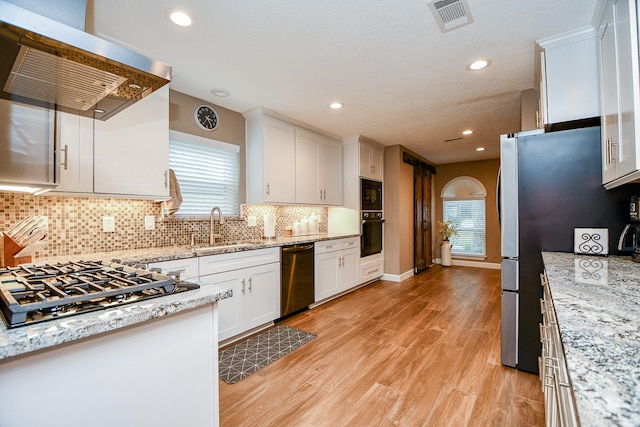 kitchen with sink, white cabinetry, light stone counters, island range hood, and black appliances