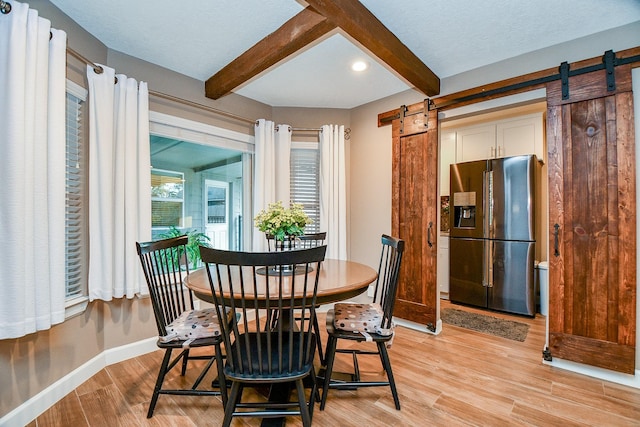 dining room featuring light hardwood / wood-style floors, a barn door, and beamed ceiling