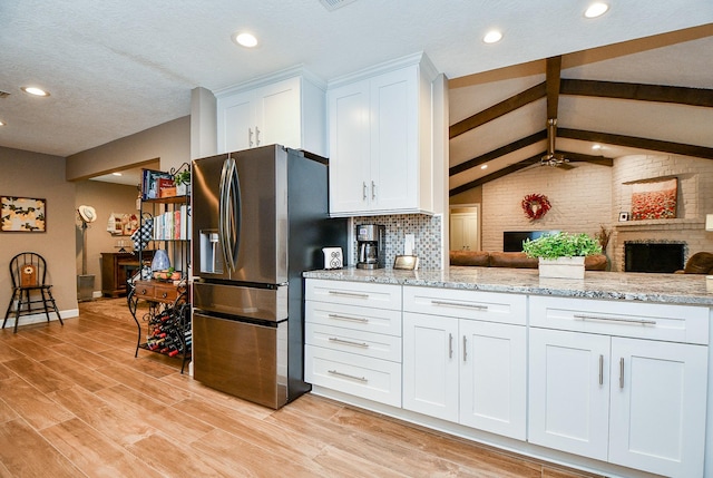 kitchen with lofted ceiling with beams, white cabinetry, stainless steel refrigerator with ice dispenser, light stone countertops, and light hardwood / wood-style flooring