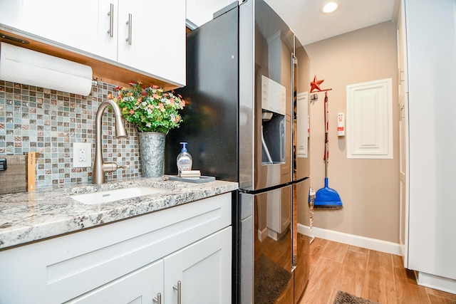 kitchen featuring light stone counters, sink, tasteful backsplash, and white cabinets