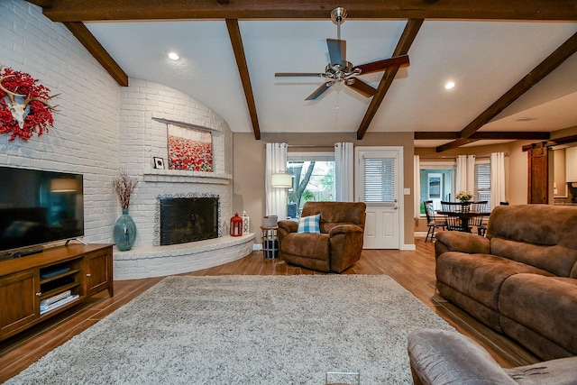 living room featuring a brick fireplace, hardwood / wood-style flooring, lofted ceiling with beams, and ceiling fan