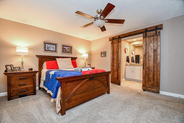 bedroom with a barn door, connected bathroom, carpet, and a textured ceiling