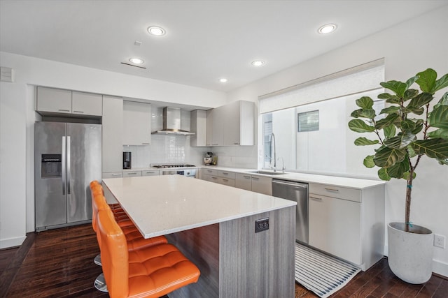 kitchen featuring appliances with stainless steel finishes, dark wood-type flooring, sink, wall chimney range hood, and a center island