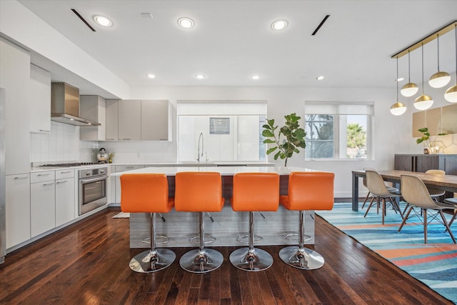 kitchen featuring sink, dark wood-type flooring, wall chimney range hood, backsplash, and appliances with stainless steel finishes