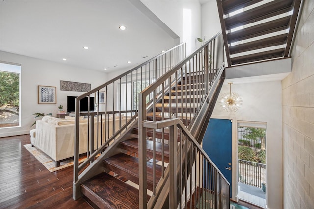 stairs with wood-type flooring, a towering ceiling, and a notable chandelier