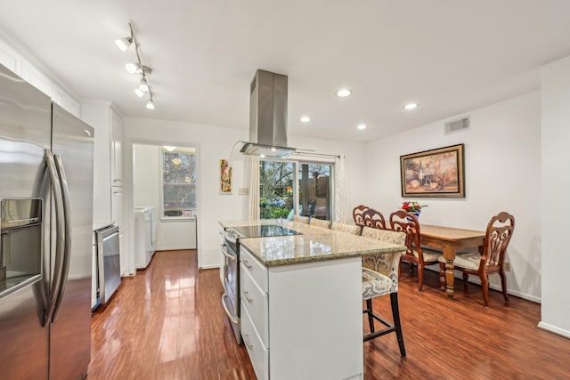 kitchen featuring a kitchen island, appliances with stainless steel finishes, island range hood, wood-type flooring, and a breakfast bar area